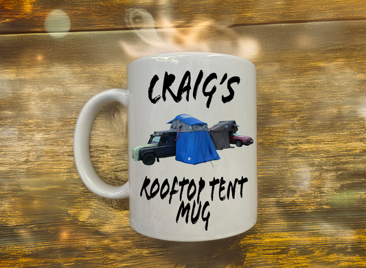 White mug with 'Craig's Rooftop Tent Mug' text and graphics on a wooden background