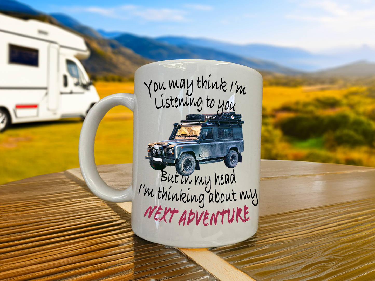 Mug with text and Landrover defender illustration on a wooden table with a scenic background