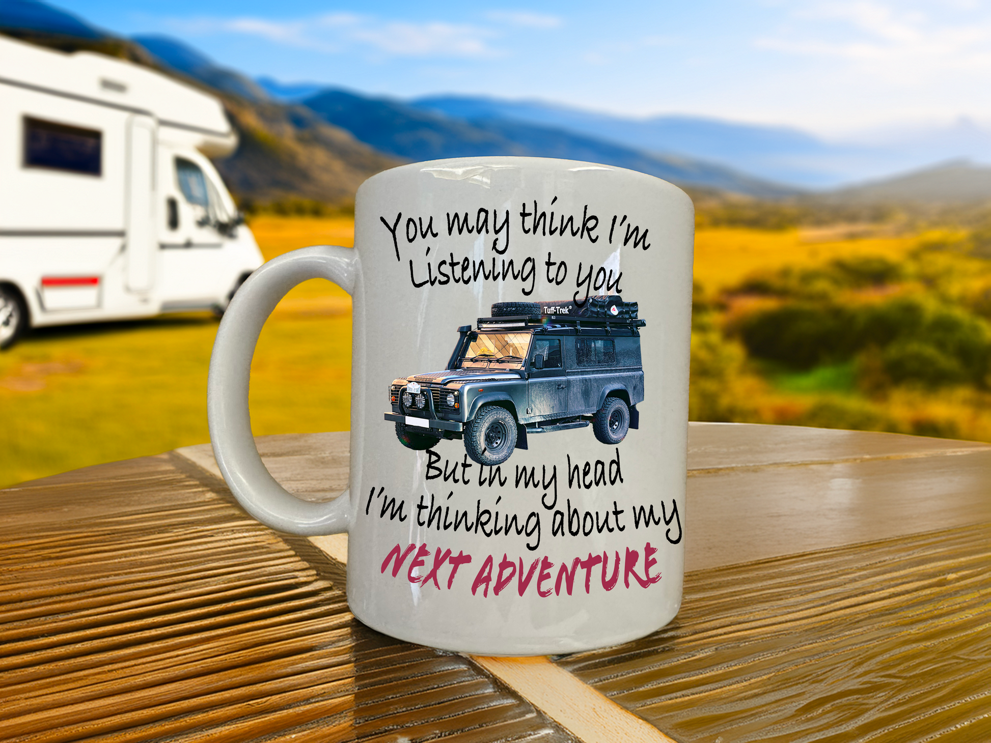 Mug with text and Landrover defender illustration on a wooden table with a scenic background