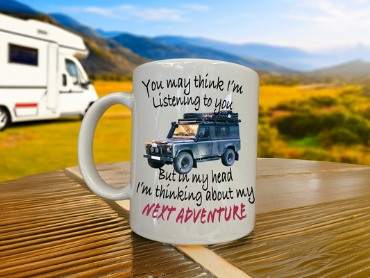 Mug with text and Landrover defender illustration on a wooden table with a scenic background