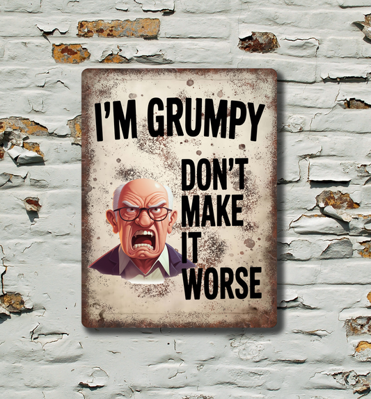 A rectangular metal tin sign with a distressed vintage look, featuring a grumpy cartoon man and the text 'I'M GRUMPY DON'T MAKE IT WORSE'. The sign is displayed on a white brick wall with peeling paint.