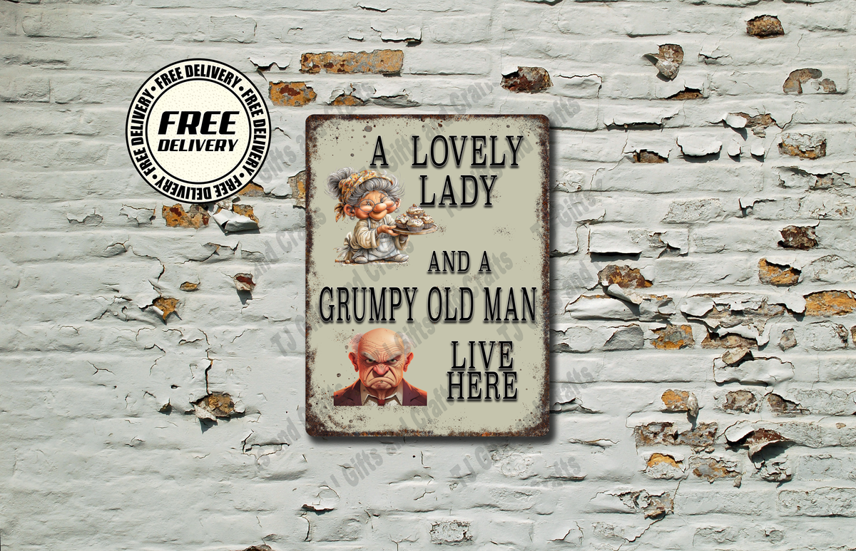 A rectangular vintage-style metal sign with a distressed cream background and black text reading 'A LOVELY LADY AND A GRUMPY OLD MAN LIVE HERE,' displayed against a white brick wall with peeling paint. The sign includes small illustrated portraits and a circular 'FREE DELIVERY' badge appears in the upper left.