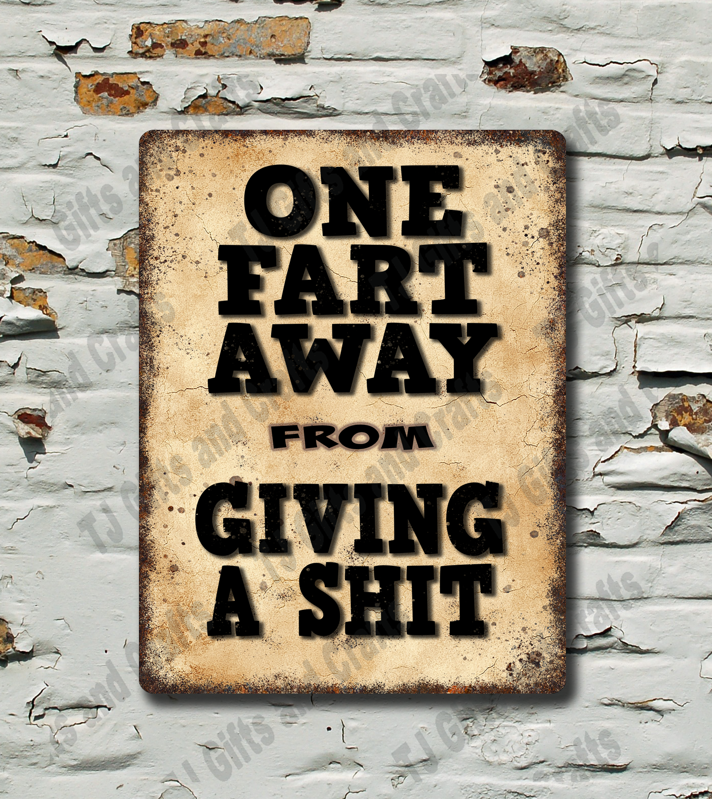 A rectangular vintage-style metal sign with distressed beige and brown tones, featuring bold black text that reads 'ONE FART AWAY FROM GIVING A SHIT,' mounted against a white brick wall with peeling paint.