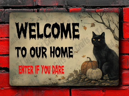 A rectangular Halloween-style wall sign mounted on a red brick wall. The sign reads 'WELCOME TO OUR HOME' in black letters with 'ENTER IF YOU DARE' in red at the bottom, and it includes an illustration of a black cat, pumpkins, and bare branches.