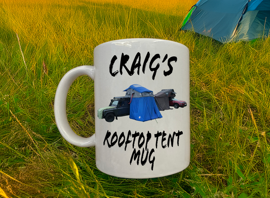 White mug with 'Craig's Rooftop Tent Mug' text and graphics on grass with a tent in the background