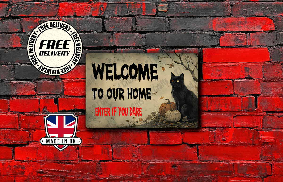A rectangular decorative sign with a distressed beige background, featuring the text 'WELCOME TO OUR HOME ENTER IF YOU DARE' in black and red, alongside an illustration of a black cat, pumpkins, and autumn leaves. The sign is displayed against a red and black brick wall backdrop, with promotional badges for 'FREE DELIVERY' and 'MADE IN UK' on the left.