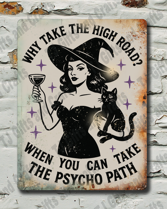 A rectangular vintage-style metal tin sign with a witch illustration and the text 'WHY TAKE THE HIGH ROAD? WHEN YOU CAN TAKE THE PSYCHO PATH' is mounted on a distressed white brick wall.
